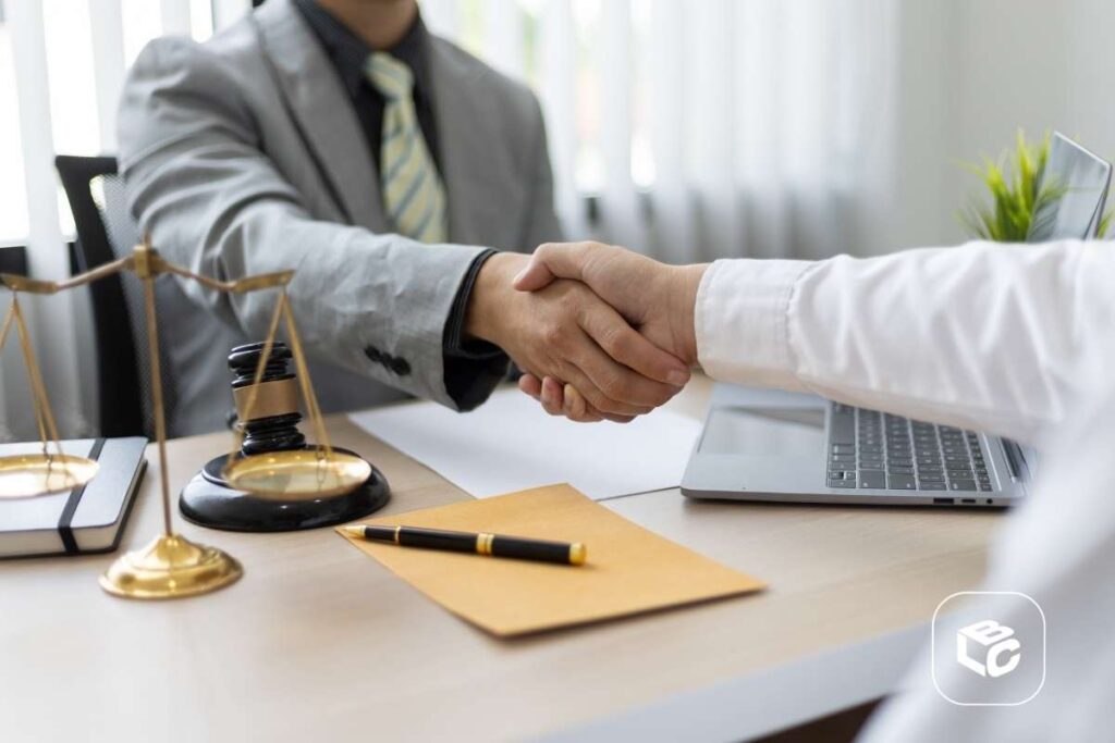 Cliente e representante jurídico apertando as mãos em escritório, com balança da justiça, martelo de juiz e notebook sobre a mesa, simbolizando acordo e antecipação de crédito judicial.