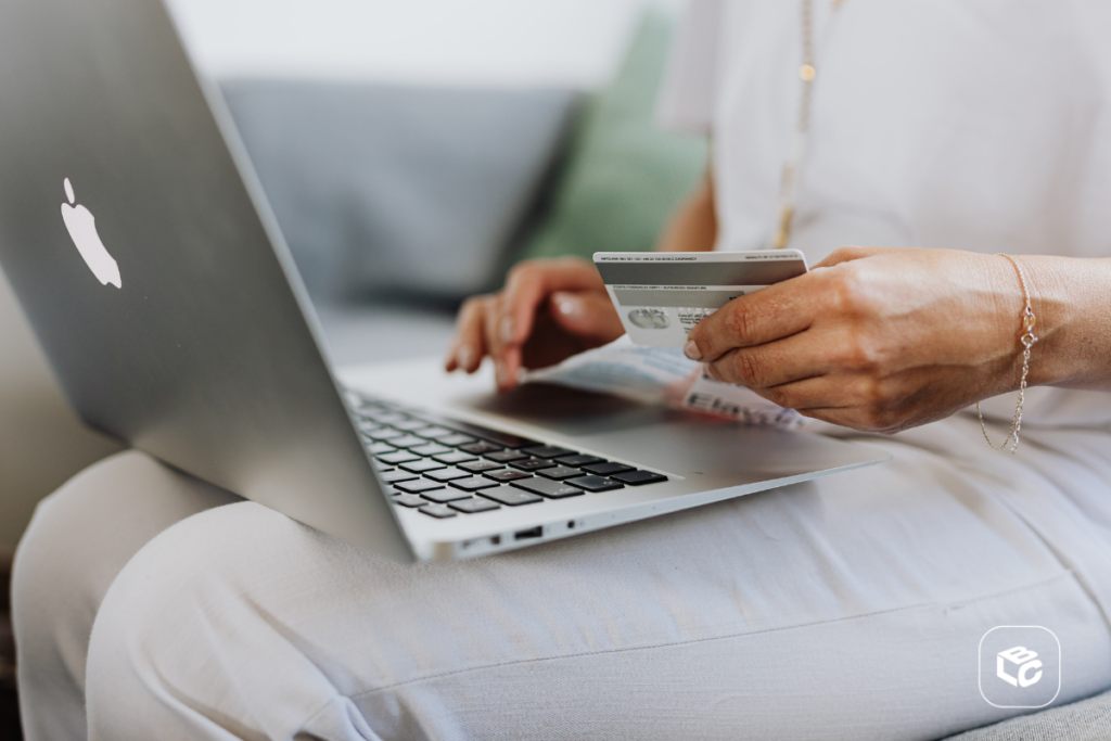 Notebook no colo de uma pessoa fazendo consulta com o cartão de crédito na mão