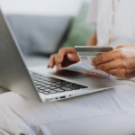 Notebook no colo de uma pessoa fazendo consulta com o cartão de crédito na mão